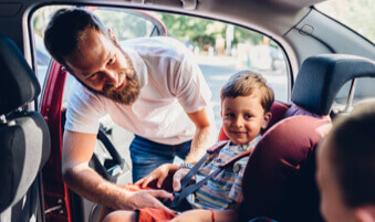 Father buckling young child into a car seat