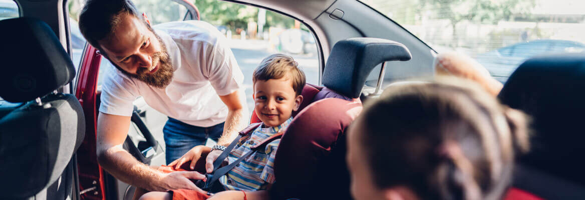 Father buckling young child into a car seat