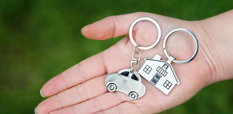 Close-up of a hand holding a car-shaped keychain and a home-shaped keychain